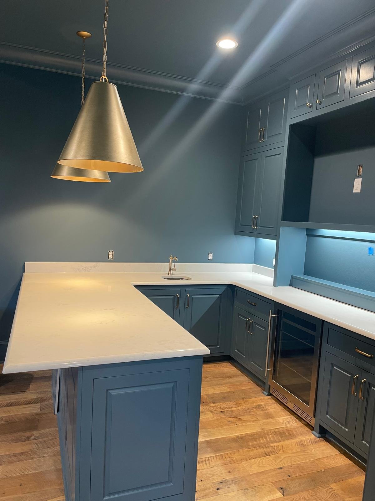 Dark blue wet bar with brass pendants and quartz waterfall