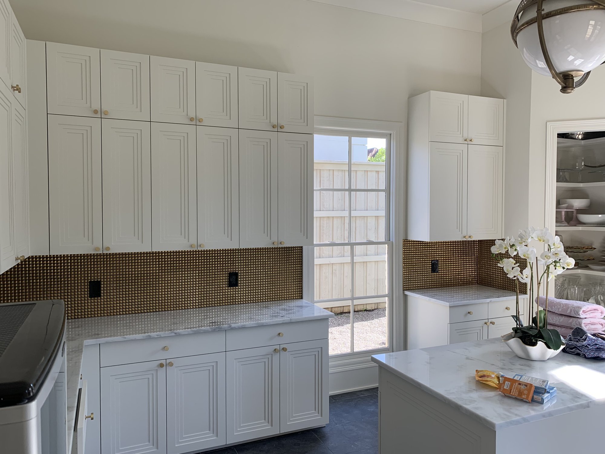Bright laundry room with white cabinetry, gold mosaic backsplash, and marble counters